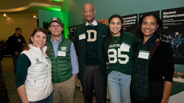 Five people wearing Dartmouth gear with arms around each other posing for a photo.