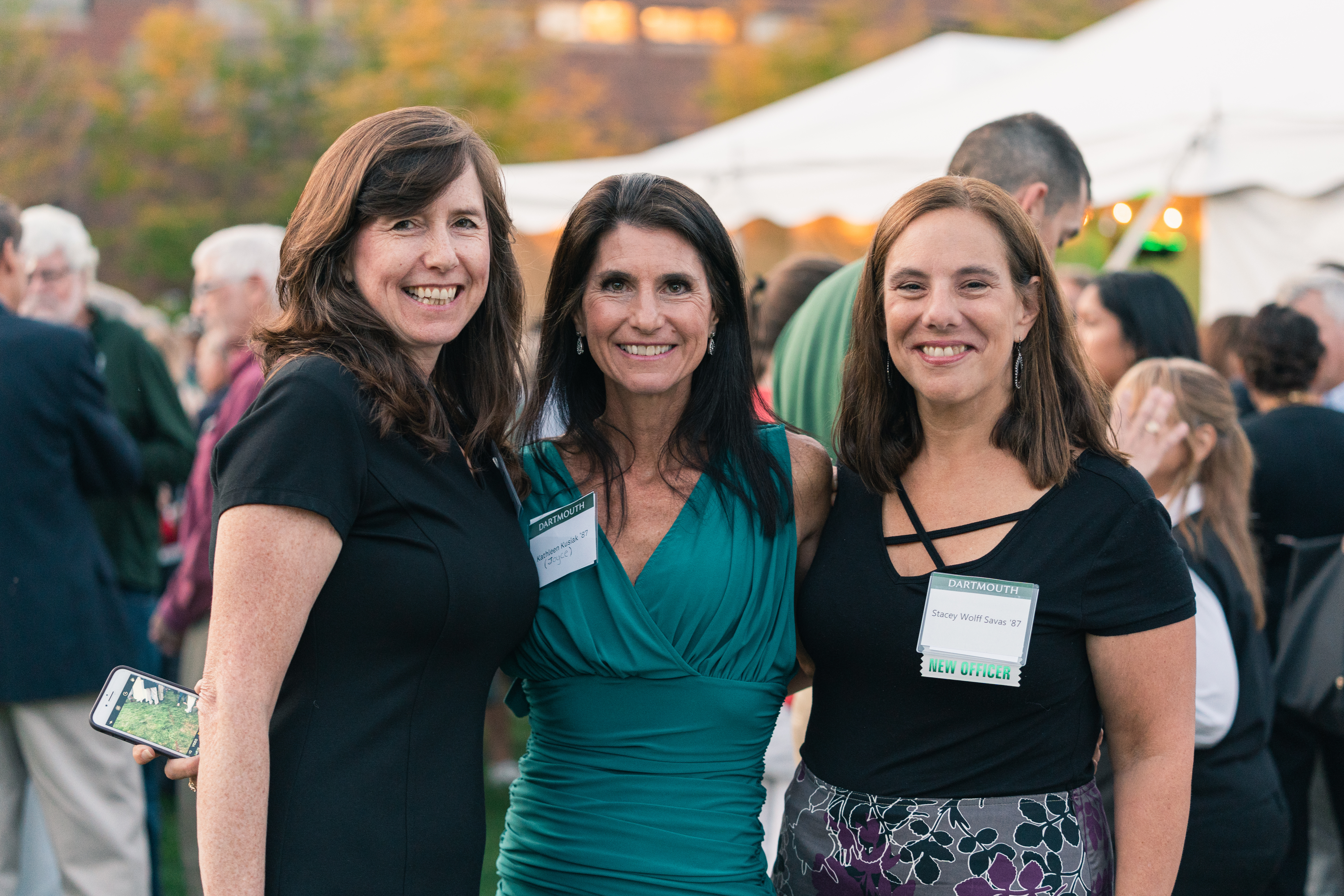 Three women in dresses and nametags smiling at the camera.