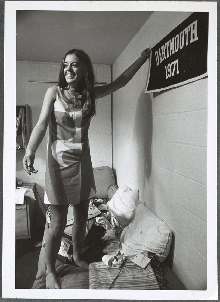 A female student hanging a Dartmouth 1971 banner on a wall in a dorm room